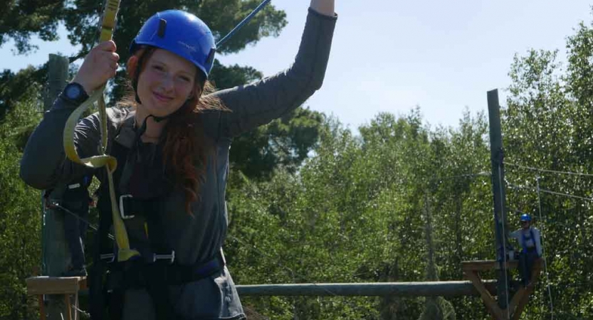 a student smiles while participating in a ropes course with outward bound